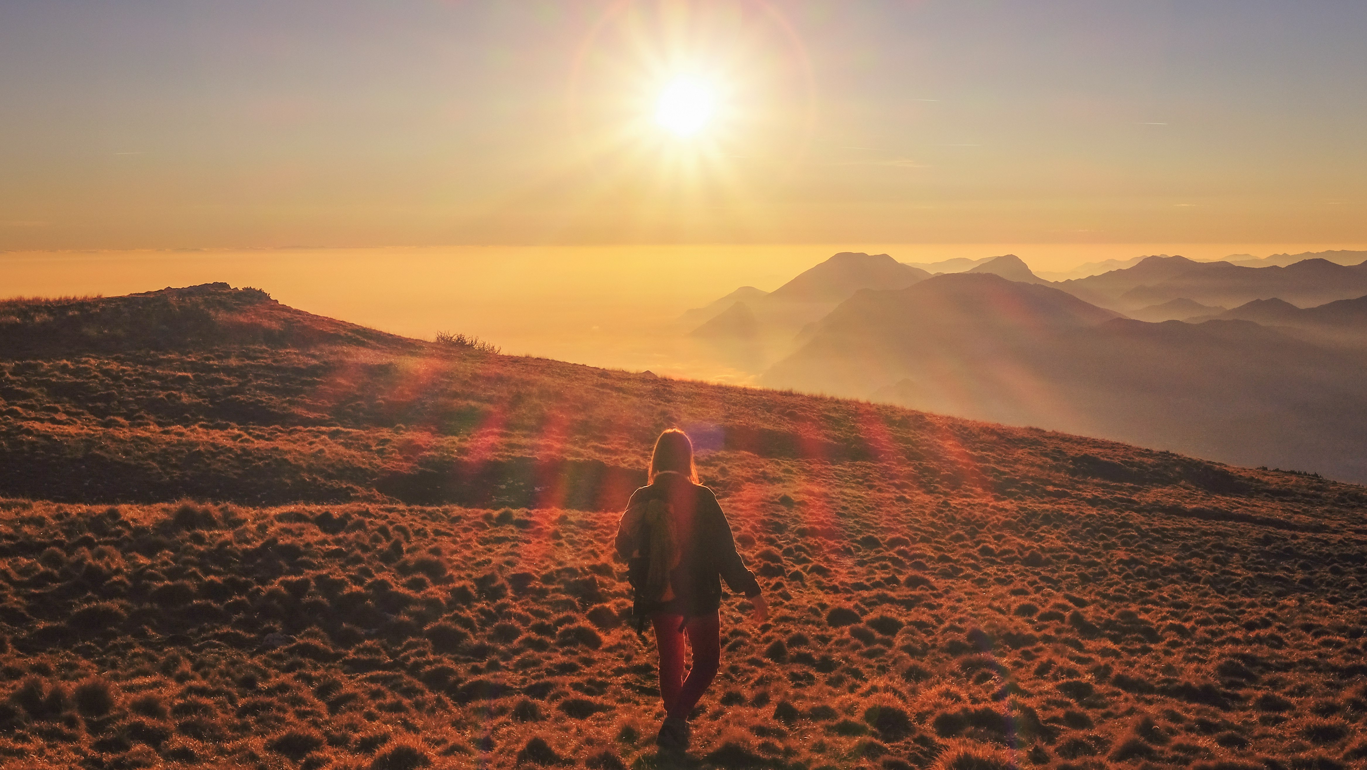 woman in blue jacket walking on desert during sunset